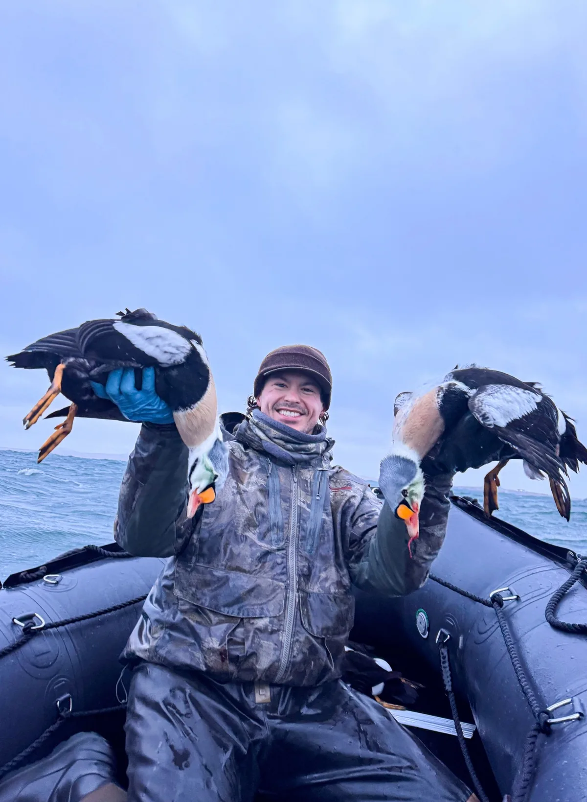 Heath Hoogerhyde, founder of All Feathers Taxidermy, holding two king eiders in a boat on open water