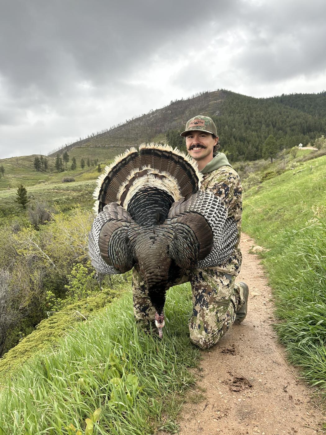 Heath Hoogerhyde, founder of All Feathers Taxidermy, kneeling with a harvested wild turkey